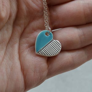 May include: A silver chain necklace with a blue and white ceramic heart pendant. The heart is divided diagonally, with one half painted blue and the other half with white stripes.
