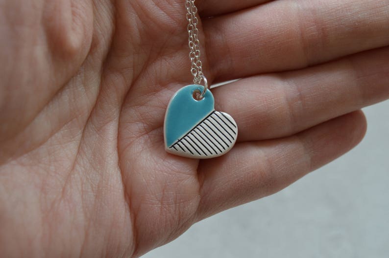 May include: A silver chain necklace with a blue and white ceramic heart pendant. The heart is divided diagonally, with one half painted blue and the other half with white stripes.