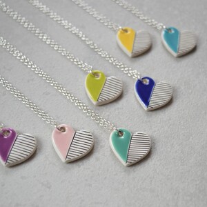 May include: Seven silver necklaces with ceramic heart pendants. Each heart is half white with black stripes and half a different colour: purple, pink, teal, blue, yellow, green, and turquoise.