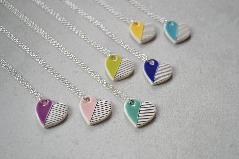 May include: Seven silver necklaces with ceramic heart pendants. Each heart is half white with black stripes and half a different colour: purple, pink, teal, blue, yellow, green, and turquoise.