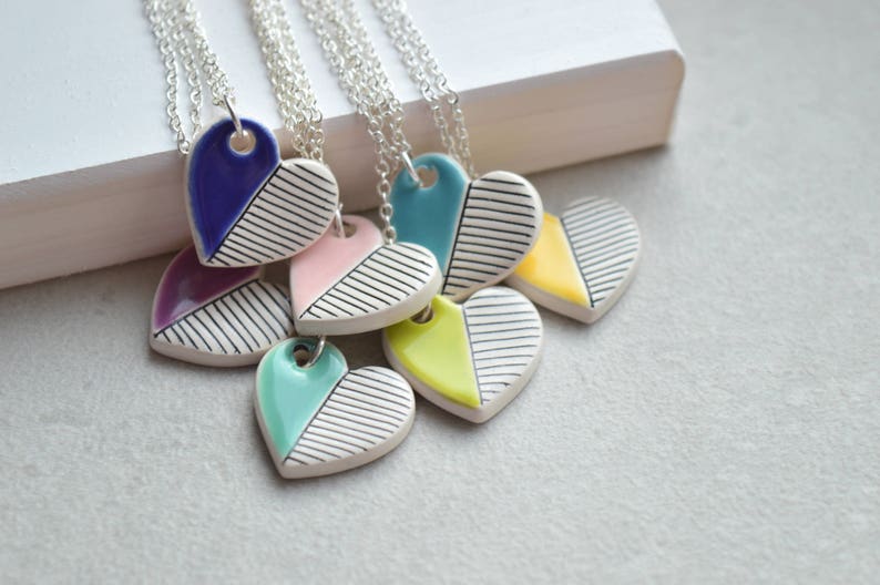 May include: A set of six ceramic heart necklaces with black and white striped patterns. Each heart is a different colour: purple, pink, turquoise, blue, yellow, and green.