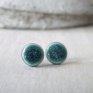 Op de afbeelding: Een paar kleine, ronde, tealblauwe oorbel studs met een glinsterende, gespikkelde afwerking.