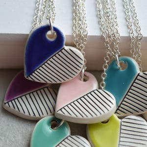 May include: A set of six ceramic heart necklaces with silver chains. Each heart is painted with a different colour and has a black and white striped pattern.