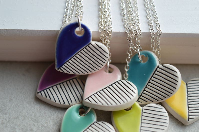 May include: A set of six ceramic heart necklaces with silver chains. Each heart is painted with a different colour and has a black and white striped pattern.
