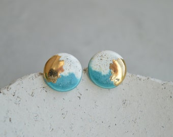 May include: A pair of round ceramic earrings with a white and blue glaze and gold accents. The earrings have a textured surface.