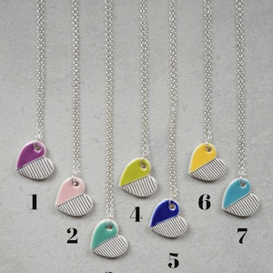 May include: Seven silver necklaces with different coloured heart pendants. The hearts are white with black stripes and a coloured top half. The colours are purple, pink, teal, yellow, blue, yellow, and teal.