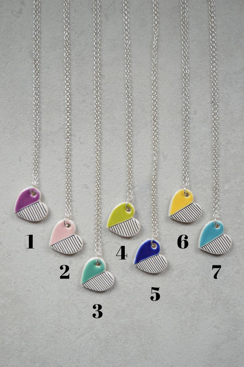 May include: Seven silver necklaces with different coloured heart pendants. The hearts are white with black stripes and a coloured top half. The colours are purple, pink, teal, yellow, blue, yellow, and teal.