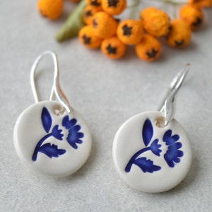 May include: A pair of ceramic earrings with a blue floral design on a white background. The earrings are attached to silver hooks.