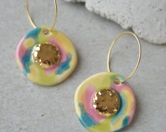 May include: A pair of gold hoop earrings with yellow, pink, and blue ceramic charms. Each charm has a gold textured circle in the center.