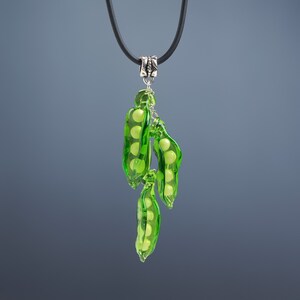 May include: A green glass necklace with a pendant of three pea pods filled with small, white beads. The necklace is on a black cord with a silver clasp.