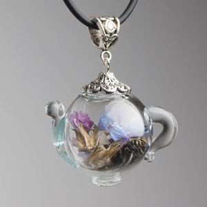 Może przedstawiać: Srebrny naszyjnik z zawieszką w kształcie czajnika z szklaną bańką zawierającą suszone kwiaty. Kwiaty są fioletowe, niebieskie i białe.