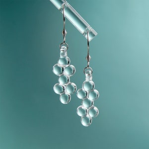 Könnte beinhalten: Ein Paar silberne Ohrringe mit klaren Glasperlen. Die Perlen sind in einer Traube angeordnet, die an Trauben erinnert.