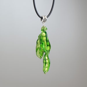 May include: A green glass pea pod necklace with a black cord and silver clasp. The pea pod is filled with white glass peas.