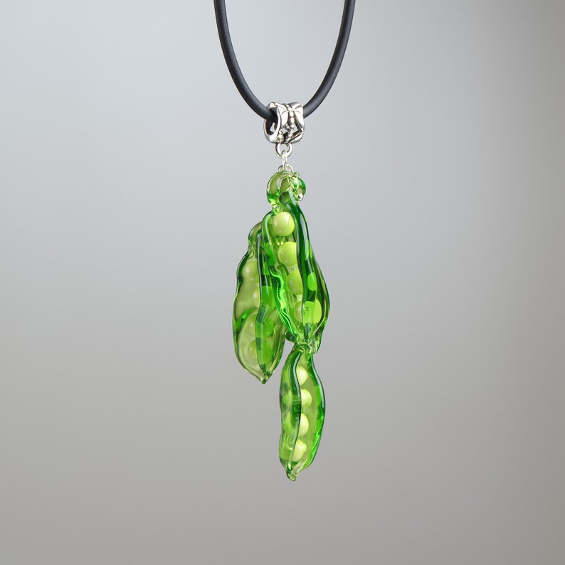 May include: A green glass pea pod necklace with a black cord and silver clasp. The pea pod is filled with white glass peas.