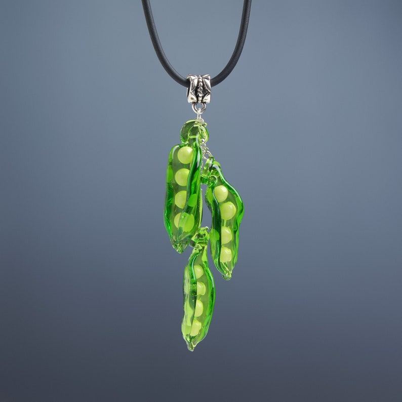 May include: A green glass necklace with a pendant of three pea pods filled with small, white beads. The necklace is on a black cord with a silver clasp.