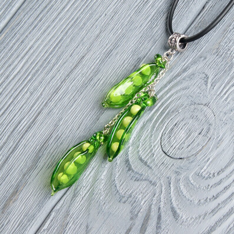 May include: A green glass pea pod necklace with a black cord and silver chain. The pea pods are filled with small white beads.