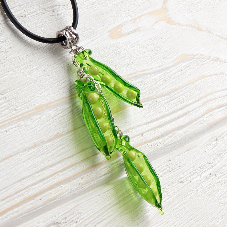 May include: A green glass pea pod necklace with a silver chain and black cord. The pea pods are filled with green glass peas.