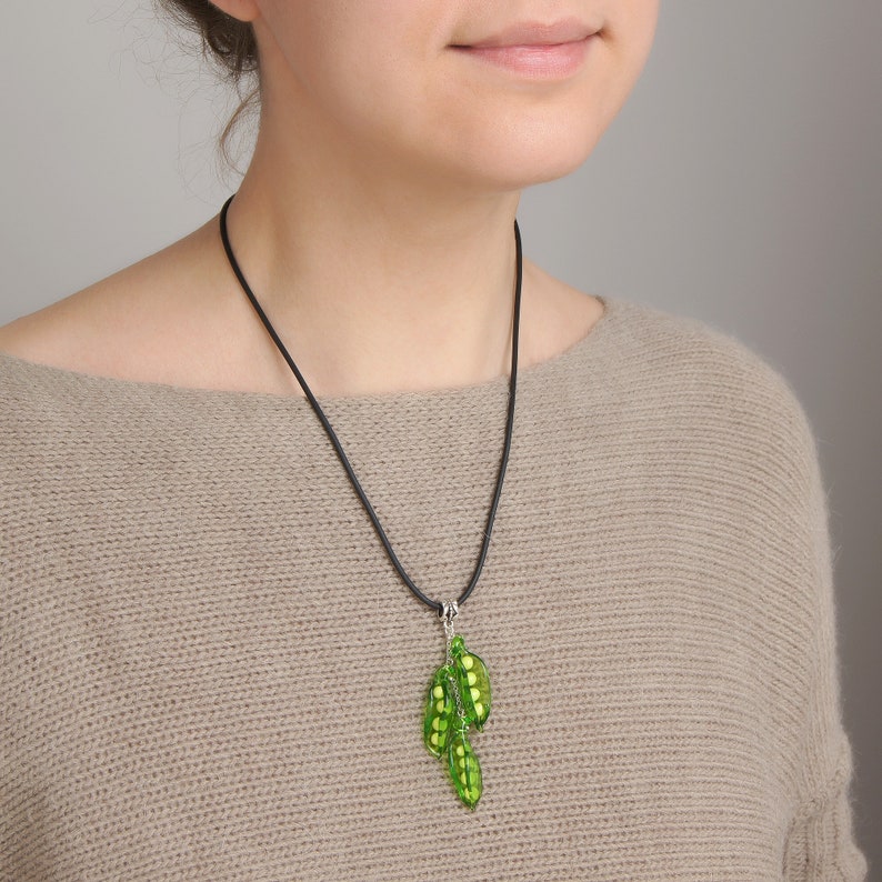 May include: A green pea pod necklace with a black cord. The necklace features three pea pods with white beads inside.