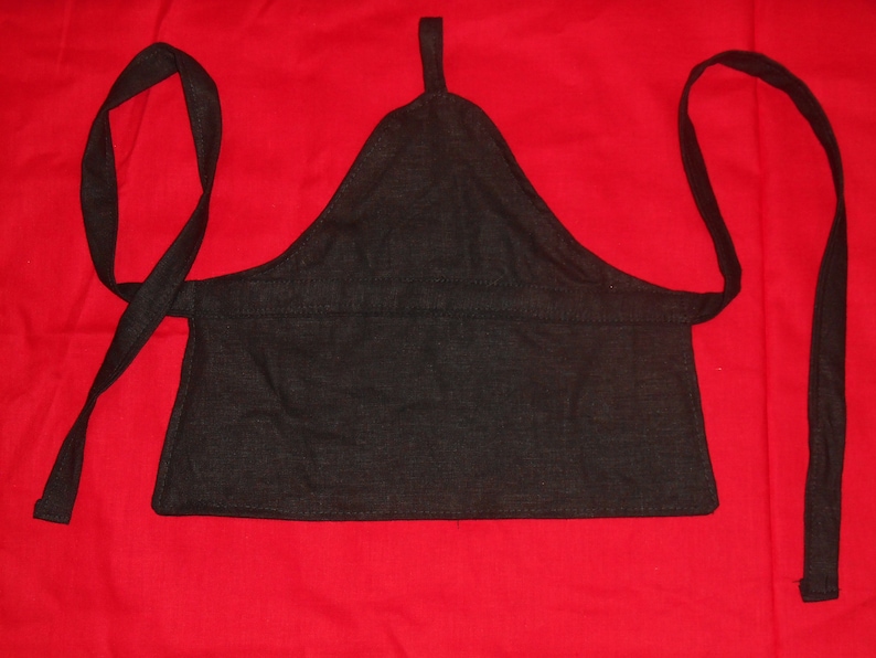 May include: A black fabric apron with two long ties. The apron has a triangular shape at the top and a straight bottom edge.
