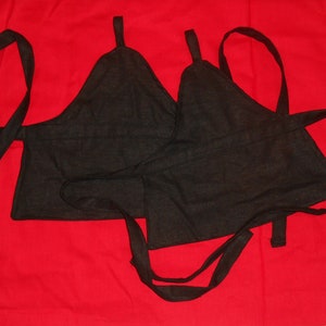 May include: Two black fabric halter tops with adjustable straps. The tops are made of a soft, woven fabric and have a simple, minimalist design.