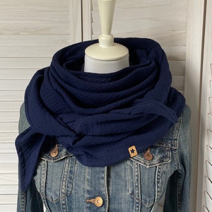 Könnte beinhalten: Ein marineblauer Schal aus Baumwolle mit einem kleinen sternförmigen Anhänger. Der Schal ist gefaltet und um den Hals einer Schaufensterpuppe gelegt.