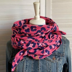 Könnte beinhalten: Ein pinkfarbener und marineblauer Schal mit Leopardenmuster ist um einen Schaufensterpuppenkopf drapiert. Der Schal ist aus einem weichen Stoff gefertigt und vorne geknotet. Der Schal wird mit einer Jeansjacke kombiniert.