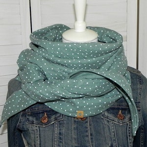 Könnte beinhalten: Ein grün-weiß gepunkteter Schal aus weichem Stoff. Der Schal ist gefaltet und um den Hals einer Puppe gelegt.