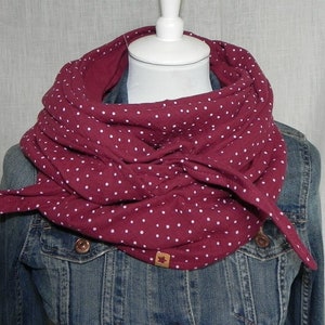 Könnte beinhalten: Ein burgunderfarbener Infinity-Schal mit weißen Punkten. Der Schal ist aus einem weichen, bequemen Stoff gefertigt und perfekt, um sich im Winter warm zu halten.