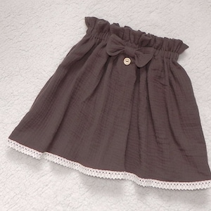 Könnte beinhalten: Ein brauner Rock mit weißem Spitzenbesatz und einer braunen Schleife an der Taille. Der Rock hat einen Knopfverschluss und ist aus einem weichen, bequemen Stoff gefertigt.