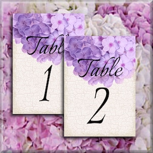 May include: Two purple floral table number cards with a white background. The first card says "Table 1" and the second card says "Table 2".