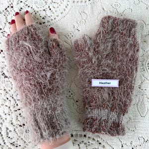 May include: A pair of heather-colored fingerless gloves. The gloves are made of a soft, fuzzy material with a mix of brown and white fibers. The label on the glove reads "Heather".