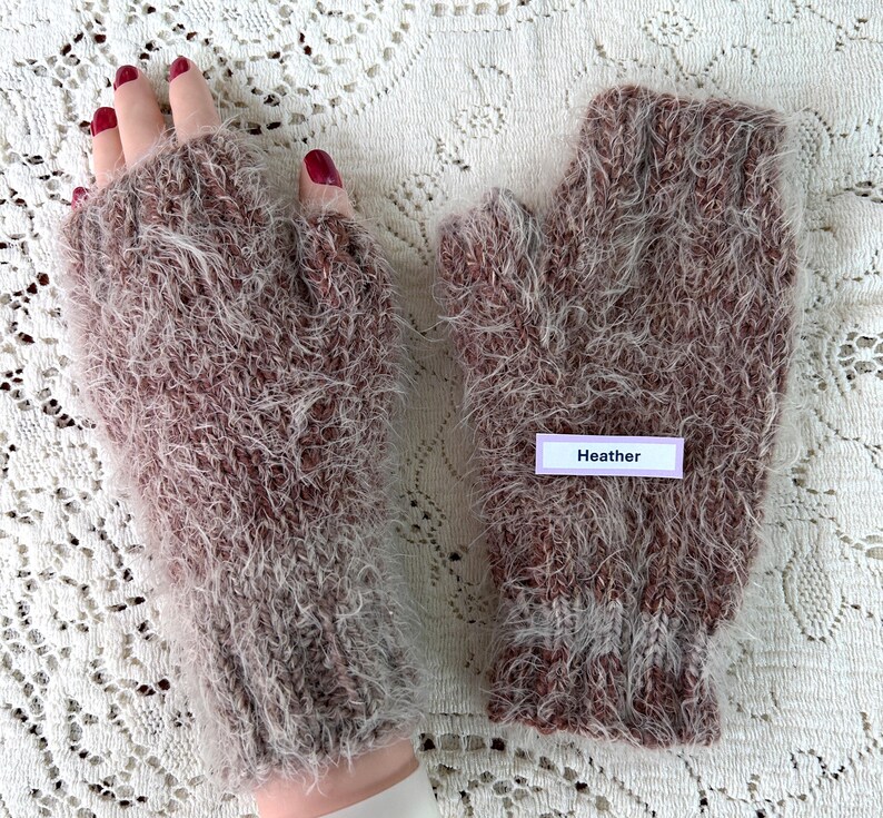 May include: A pair of heather-colored fingerless gloves. The gloves are made of a soft, fuzzy material with a mix of brown and white fibers. The label on the glove reads "Heather".