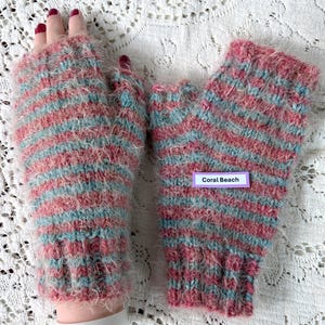 May include: A pair of fingerless gloves in a coral, light blue, and white striped pattern. The gloves are made of a fuzzy, soft material. The label on the gloves reads "Coral Beach".