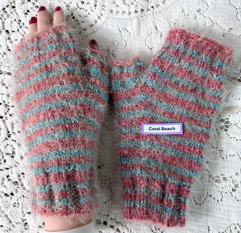 May include: A pair of fingerless gloves in a coral, light blue, and white striped pattern. The gloves are made of a fuzzy, soft material. The label on the gloves reads "Coral Beach".