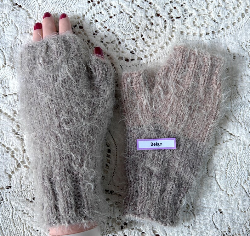 May include: A pair of beige fingerless gloves made of a soft, fuzzy material. The gloves are a light beige color with a label that reads "Beige". The gloves are designed to keep hands warm while leaving fingers free.