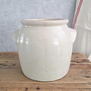 May include: A white ceramic mug with a black handle and the text "But First, Coffee" in a bold, black font. The mug is sitting on a wooden surface. The mug is approximately 4 inches tall.