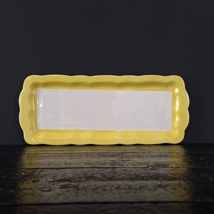 以下が含まれることがあります： 波打つ縁のある黄色いセラミック製のサービングトレイ。トレイの内側は白で、スナックやアペタイザーを盛り付けるのに最適です。