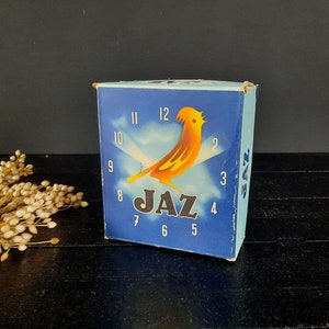May include: A blue box with a yellow bird and a clock face on it. The box says "JAZ" on it.