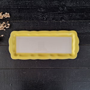 以下が含まれることがあります： 波打つ縁のある黄色いセラミック製のサービングトレイ。トレイは空で、内側は白です。