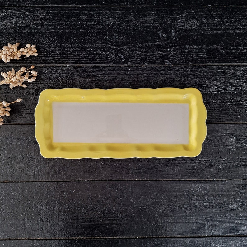以下が含まれることがあります： 波打つ縁のある黄色いセラミック製のサービングトレイ。トレイは空で、内側は白です。