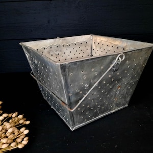 Puede incluir: Un colador cuadrado de metal plateado vintage con un asa de alambre. El colador tiene un diseño perforado y está ligeramente abollonado.