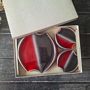 Puede incluir: Un juego de tres fuentes de cerámica para servir en una caja de regalo. Las fuentes son rojas, grises y blancas, con un diseño curvo único. El juego incluye una fuente ovalada grande y dos fuentes más pequeñas a juego.