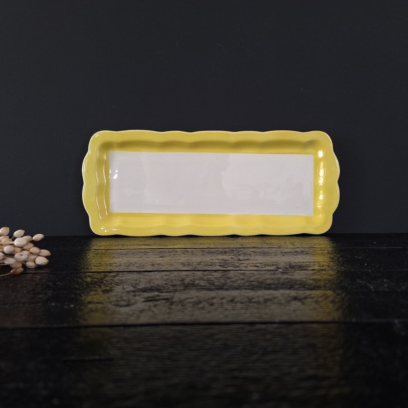 以下が含まれることがあります： 波打つ縁のある黄色いセラミック製のサービングトレイ。トレイの内側は白で、スナックやアペタイザーを盛り付けるのに最適です。
