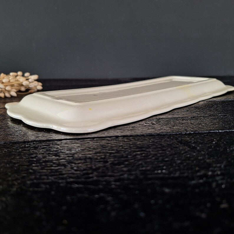 以下が含まれることがあります： 縁が波打った白いセラミック製のサービングトレイ。トレイは空で、黒い表面の上に置かれています。
