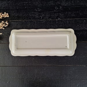 以下が含まれることがあります： 波打った縁のある白い長方形のセラミック製サービングディッシュ。ディッシュは滑らかで光沢のある仕上げで、底に「5」のマークが付いています。