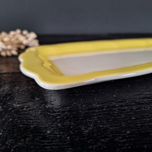 以下が含まれることがあります： 波打つ縁取りのある小さな長方形のセラミック皿。皿は黄色で、内側は白です。