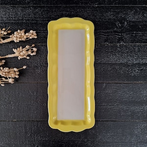 May include: A yellow ceramic serving dish with a white interior. The dish has a scalloped edge and is perfect for serving snacks or appetizers.