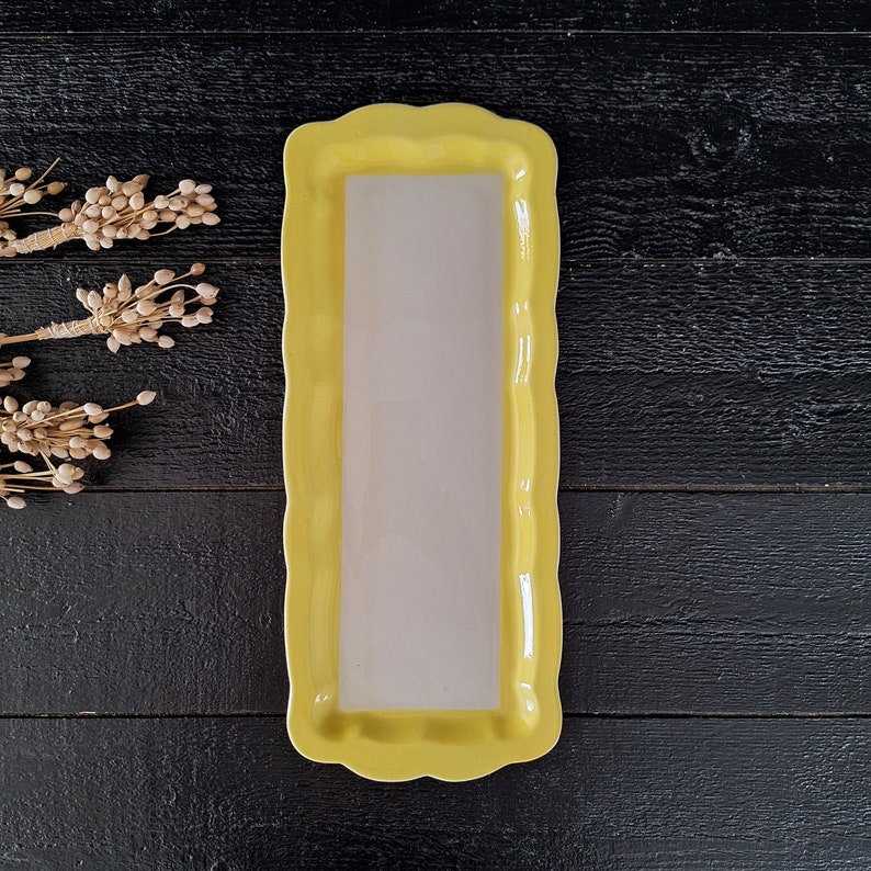 以下が含まれることがあります： 白い内側を持つ黄色いセラミック製のサービングディッシュ。ディッシュは波状のエッジになっており、スナックやアペタイザーを提供するのに最適です。