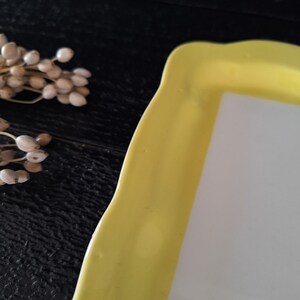 以下が含まれることがあります： 白い内側を持つ黄色いセラミック製のサービングトレイ。トレイは波状のエッジになっており、スナックやアペタイザーを提供するのに最適です。