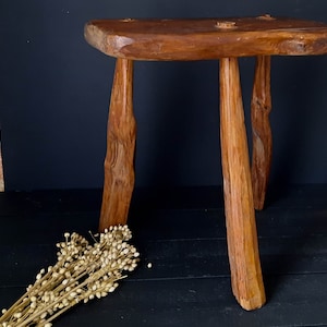 May include: A rustic wooden stool with three legs. The stool is made of natural wood and has a simple, handcrafted design.